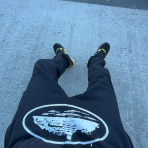 Corteiz byxor i strl XS/S - Snygga svarta mjukisbyxor med ett coolt vitt tryck framtill. Byxorna har en elastisk midja och är perfekta för en avslappnad stil. De är bekväma och lätta att bära.