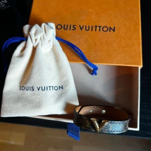 Louis Vuitton armband  - Säljer ett elegant brunt armband från Louis Vuitton med gulddetaljer. Armbandet har en stilren design med ett V-format guldfärgat spänne och justerbara tryckknappar. Perfekt för att ge en lyxig touch till din outfit.                              Skriv om ni har några frågor eller funderingar 😊
