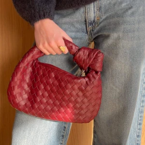 Röd flätad handväska - Snygg röd handväska med flätat mönster och knutdetalj på handtaget. Snygg färgklick. Är från design by si, ”Florence bag mini” i en vinröd färg. Nypris 514 kr.