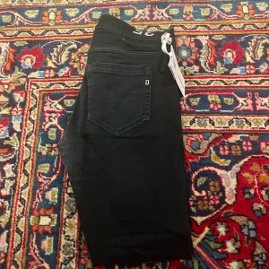 Svarta jeans från Dondup - Snygga svarta jeans från Dondup med en klassisk femficksdesign. Byxorna har en knappgylf och en stilren look som passar perfekt till olika tillfällen. Märkeslogga på bakfickan ger en extra touch.