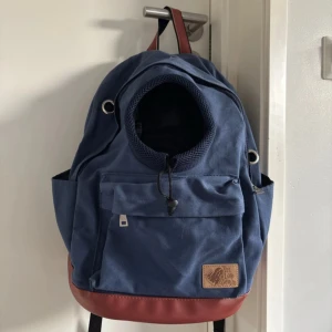 Blå ryggsäck för hund från Pet Love Denim - Säljer en snygg blå ryggsäck för hund/katt från Pet Love Denim med bruna detaljer. Ryggsäcken har en praktisk dragkedja framtill och justerbara axelremmar. Aldrig använd