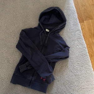 Mörkblå hoodie med fjärilsbroderi - Säljer en snygg mörkblå hoodie med dragkedja och en cool rosa fjärilsbroderi på framsidan. Tröjan har en justerbar huva med snören och långa ärmar. Den passar både xs och s! Kanske även m