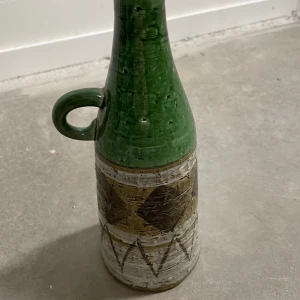 Grön och brun keramikvas med handtag - Unik keramikvas i grönt och brunt med ett praktiskt handtag. Vasen har ett rustikt mönster med geometriska former och en glaserad yta som ger en fin glans. Perfekt som dekorativt inslag i hemmet eller som gåva.