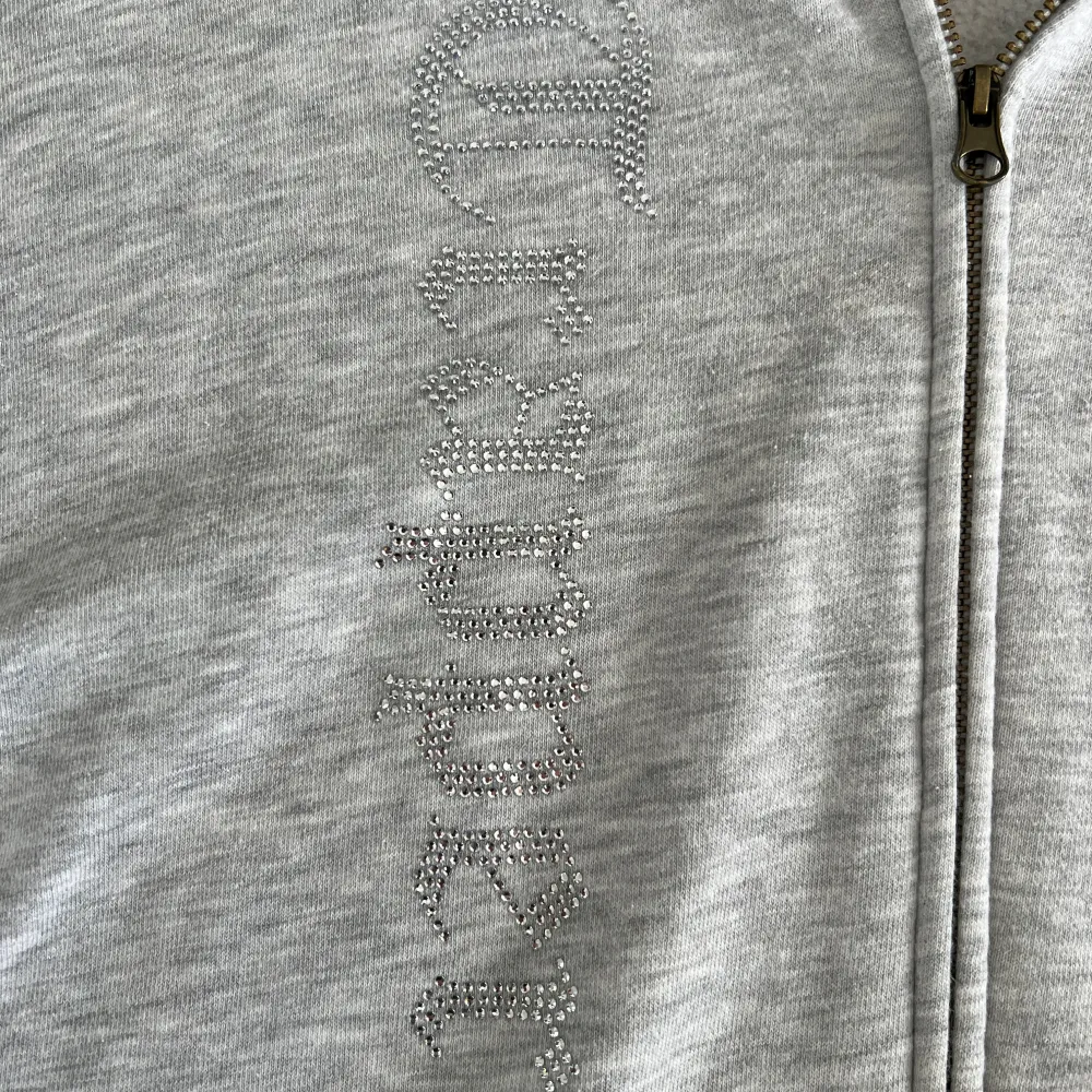 Säljer en grå hoodie med dragkedja och ett coolt ormmönster i svart på framsidan. Tröjan har en luva och praktiska fickor framtill. Perfekt för en avslappnad stil. Tröjan är från madebytrappers . Neuletakit & Villapaidat.