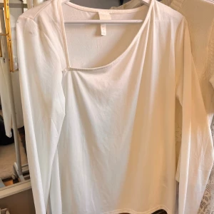 Vit långärmad topp - Säljer en stilren vit långärmad topp med rund, asymmetrisk halsringning. Enkel och mångsidig design som passar till många olika outfits. Aldrig använd. Från H&M. Storlek L men kan även användas som M.