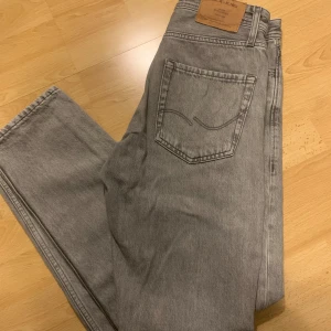 Grå jeans från Jack & Jones - Snygga grå jeans från Jack & Jones i modellen Loose/Chris. De har en loose passform och är perfekta för en avslappnad stil. Jeansen har en klassisk design med dragkedja och knapp framtill. Passar 50-70 kg. (Pris kan diskuteras)
