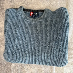 Grå ribbad tröja från Chaps - Säljer en stilren grå ribbad tröja från Chaps. Tröjan är tillverkad i 100% bomull och har en diskret broderad logga på bröstet. Perfekt för kyligare dagar med sin långärmade design och klassiska look. Passar även dem flesta som har XL.