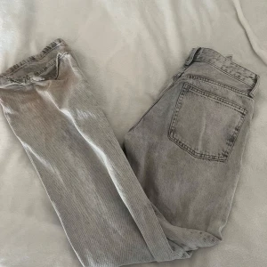 Grå jeans från Zara - Snygga grå jeans från Zara med en klassisk femficksdesign. De har en rak passform och är tillverkade i ett slitstarkt denimtyg. Perfekta för en avslappnad stil. Smutsiga längst ner och trasiga. Därav priset 