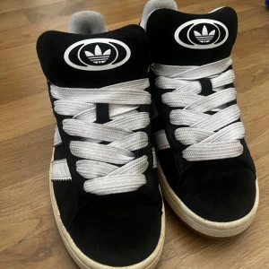 Svarta och vita campus  - Snygga svarta Adidas Campus sneakers med vita detaljer och snörning. Bara använd en sommar, kommer nu inte till så mycket andvänning. Lite slitet i ena skon, kolla sista bilden. Kommer med ett par svarta snören också.  Möjligt att de blir renare om man tvättar skorna också annars e det rätt rena  