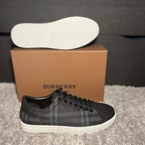 Rutig sneakers från Burberry - Snygga sneakers från Burberry med klassiskt rutigt mönster i grått och svart. Skorna har en vit sula och svart snörning. Perfekta för en stilren look.
