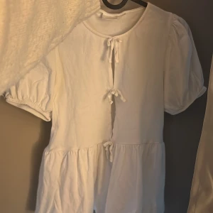Vit blus med knytband - Säljer en söt vit blus med puffiga kortärmar och knytband framtill jötte fin till alla tillfällen 