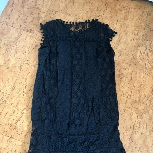 Svart spetstunika - Elegant svart spetstunika med vackra detaljer, design med spets och små bollar längs kanterna. Perfekt för en stilfull kväll.