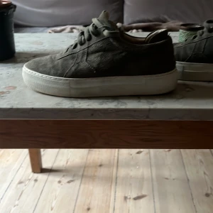 Olivgröna sneakers från Axel Arigato - Snygga olivgröna sneakers från Axel Arigato med en stilren design. Skorna har en vit sula och är tillverkade i mocka med snörning framtill. Perfekta för en avslappnad stil.