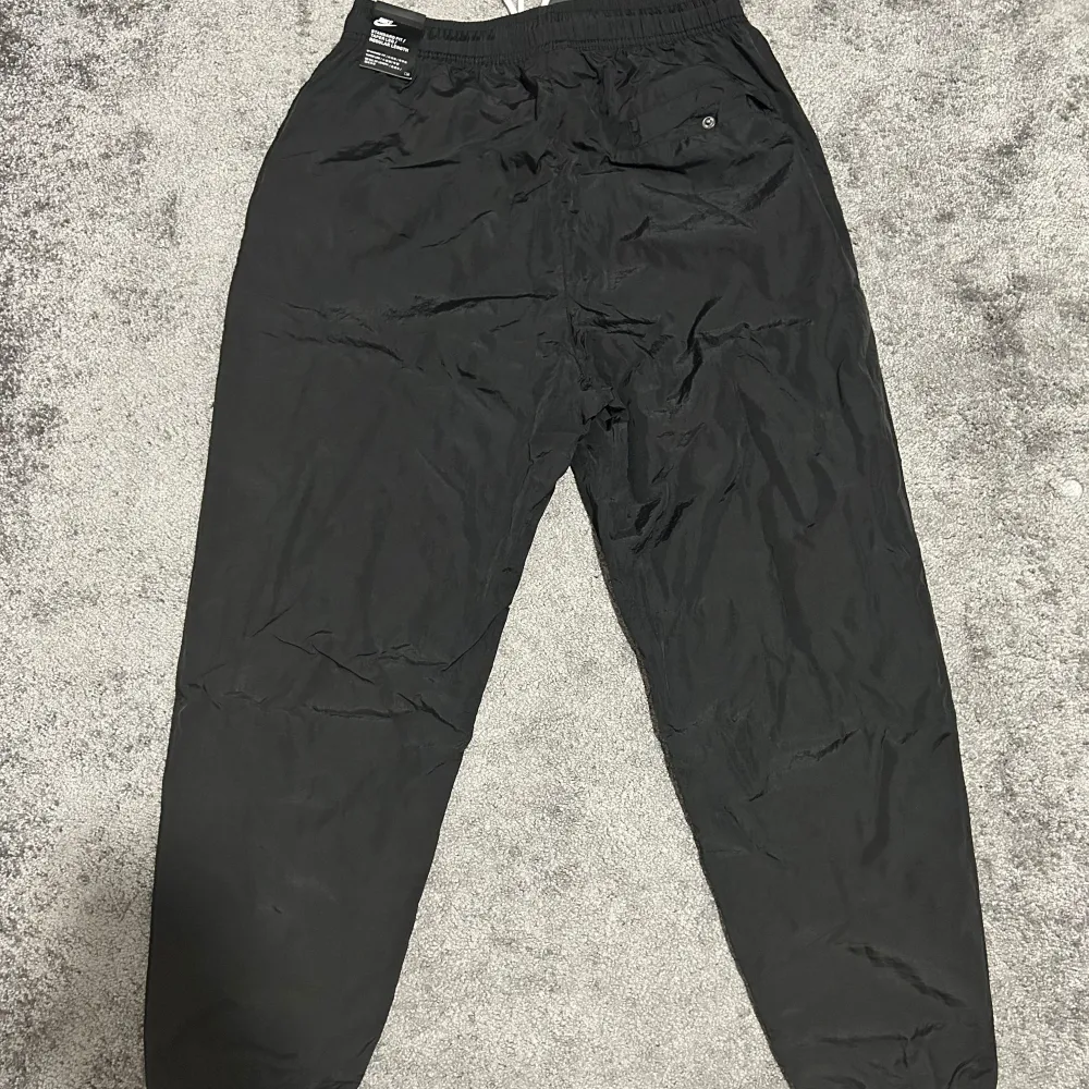 Snygga svarta träningsbyxor från Nike med vita detaljer. Byxorna har elastisk midja med snörning och vita Nike-loggor längs sidorna. Perfekta för sport och träning. Det är en windbreaker pant, har jätte bra skick 10/10. Priset kan diskuteras!. Farkut & Housut.