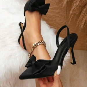 Svarta pumps med rosett - Eleganta svarta pumps med spetsig tå och en stor rosett framtill. Skorna har en smal klack och är tillverkade i ett glansigt material som ger en lyxig känsla. (Aldrig använda)