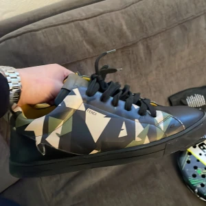 Camouflage sneakers från Fendi - Snygga sneakers från Fendi med ett unikt camouflage-mönster i gröna och svarta toner. Skorna har snörning och en bekväm passform. Perfekta för att ge din outfit en exklusiv touch. Köpta i Köpenhamn och knappt använda. Nypris 7000kr