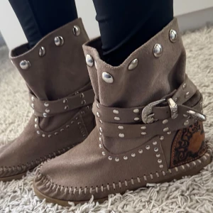 Beige bohemiska festival boots / indian minnetonka - Snygga beige bruna boots i mocka med silvriga nitar ifrån märket LDIR / L’Artigiano di Riccione. Handgjorda italienska skor som tyvärr inte görs mer, dessa är i storlek 40 men skulle passa en 39. Finns små fläckar som visas på närbild i annonsen.