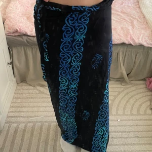 Svart och blå långkjol från Bukit Indah - Snygg svart långkjol med blått mönster från Bukit Indah. Kjolen har ett unikt mönster och knytning i midjan. Perfekt för en bohemisk stil.