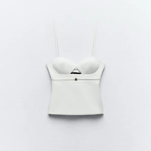 Vit korsett med smala axelband - Snygg vit korsett med smala axelband och en stilren design. Perfekt för att skapa en elegant look. Den har en liten dekorativ detalj framtill och en figurnära passform.