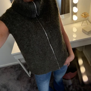 Mörkgrön stickad väst med dragkedja - Säljer en mörkgrön stickad väst med hög krage och hel dragkedja framtill. Västen är ärmlös och har en mjuk, fluffig känsla som gör den extra mysig. Perfekt att slänga över en t-shirt eller långärmad för en chill look. Köpt på weekday för 500kr, använt cirka 2 gånger