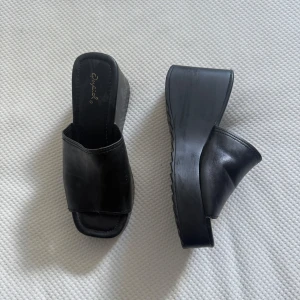 Svarta plattformssandaler  - Använt enstaka gång. Svarta sandaler med bred rem över foten och kraftig plattformssula. Snygg fyrkantig tå och öppen häl.