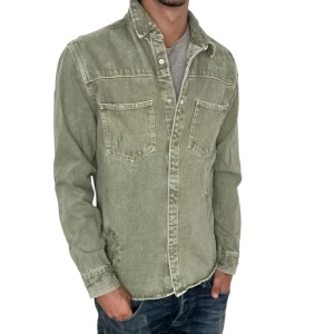Grön overshirt med slitningar  - Snygg grön overshirt med klassisk krage och två stora bröstfickor. Skjortan har långa ärmar och knäppning framtill. Materialet är robust och har en tvättad look som ger en cool vibe. Perfekt att bära över en t-shirt för en avslappnad stil.