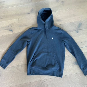 Mörkblå hoodie från Polo Ralph Lauren - Hej! Snygg mörkblå hoodie från Polo Ralph Lauren med klassisk logga broderad på bröstet. Tröjan har huva med snörning, stor magficka och långa ärmar med ribbade muddar. Perfekt för chill dagar och streetstyle. Materialet är mjuk bomull med lite stretch. Köpta i butik från USA! Andvänt mycket men väldigt sparsamt. Hör av dig vid minsta fundering! Mvh Leo. Ps pris ej hugget i sten