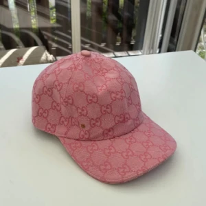 Rosa Gucci keps med GG-mönster - Snygg rosa keps från Gucci med det klassiska GG-mönstret över hela kepsen. Justerbar rem baktill i rosa läder och böjd skärm. Materialet är bomull med detaljer i läder. Perfekt för dig som vill sticka ut med en lyxig accessoar. Köpt i Italien för ungefär 3500kr säljer den för 1300kr då den inte kommer till användning. Både killar och tjejer kan använda denna! Går att pruta vid snabb affär. Hade kunnat ta 800kr