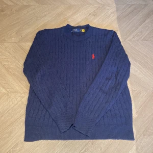 Stickad Ralph Lauren hoodie - Säljer min blåa kabelstickade tröja. Tröjan har en röd broderad logga på bröstet. Tröjan är nästintill oanvänd, pris kan diskuteras.