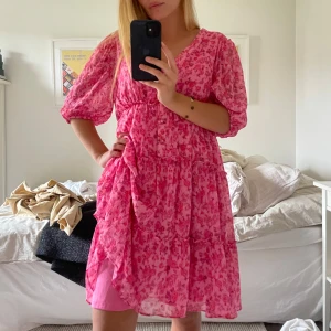 Rosa-orange blommig kortklänning med volang - Säljer en superfin rosa-orange kortklänning med blommigt mönster och volangdetaljer. Jag är 160 cm och tycker denna är liiite för lång för mig, går ungefär till knäna 😗