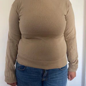 Beige långärmad tröja från Buxbom - Säljer en enkel och snygg beige långärmad tröja från Buxbom i storlek L. Tröjan är tillverkad i 100% bomull och har en rund hals samt ribbade muddar vid ärmslut och nederkant. Perfekt för dig som gillar stilrena och neutrala plagg.