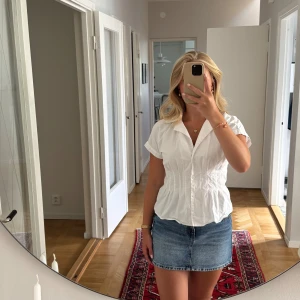 Vit blus med krage och knappar - Säljer en vit blus med korta ärmar, klassisk krage och knäppning framtill. Blusen har insydda sömmar i midjan som ger en snygg formad siluett. Perfekt att styla med jeanskjol eller byxor för en fräsch look.