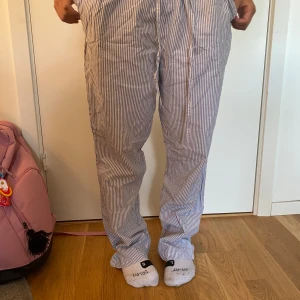 Randiga linnebyxor från 157, strl S - Säljer ett par blåvit-randiga linnebyxor från 157 i modellen Tibby Stripe. Byxorna har elastisk midja med snörning och raka ben. Perfekta för chill dagar eller när du vill ha en avslappnad look. Lätta och luftiga i materialet.