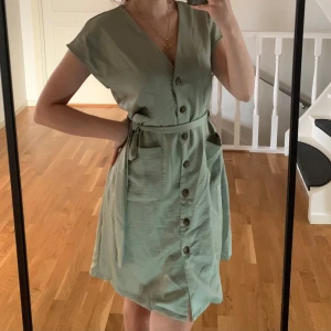 Ljusgrön klänning med knyt - Säljer en ljusgrön klänning med v-ringning, knappar framtill och knytband i midjan. Passar både xs-s