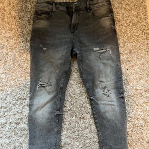 Grå slim jeans med slitningar från FSBN - Snygga grå jeans från FSBN med coola slitningar på framsidan. De har en klassisk femficksdesign och en knappgylf. Perfekta för en avslappnad stil med en edgy touch.   32/30