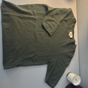 Grön kashmirtröja från KSHMR Tribu - Snygg grön stickad tröja från KSHMR Tribu i mjuk kashmir. Modellen har korta ärmar och rund halsringning med ribbad kant. Perfekt för dig som gillar stilrena och bekväma plagg med lyxig känsla. Passar dig som vill ha en enkel men ändå exklusiv look.