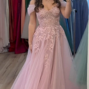 Ljusrosa långklänning med spets - Drömmig ljusrosa långklänning med offshoulder-ärmar och vackra blommiga spetsdetaljer över hela livet och kjolen. Klänningen har en romantisk, voluminös kjol i tyll och en figurnära överdel med hjärtformad urringning. Perfekt för bal eller student! Nypris 9000kr