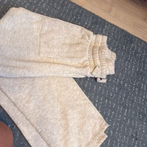 Grå mjukisbyxor med snörning, S - Säljer ett par ljusbeige mjukisbyxor från 157 i storlek S. Byxorna har bred resår och snörning i midjan, samt stora fickor både fram och bak. Perfekta för chill dagar eller när du vill vara extra bekväm. Materialet är mjukt och känns skönt mot huden. Byxan har en liten brun fläck som kanske går bort på något sätt annars är den ganska ny skick, använt tre gånger 