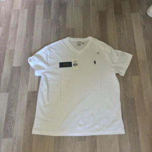 Vit v-ringad t-shirt Polo Ralph Lauren - Vit t-shirt från Polo Ralph Lauren i klassisk passform, v-ringad hals och korta ärmar. Tillverkad i mjuk bomull med den ikoniska broderade loggan på bröstet. Perfekt basic med clean look och snyggt snitt.