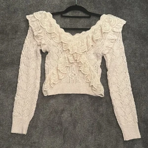 Beige stickad tröja med volang från zara - Supersöt beige stickad tröja med bred v-ringning och detaljerade volanger i spets framtill och på axlarna. Tröjan är i nyskick och säljer då den ej kommer till användning 