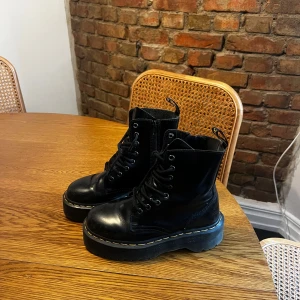 Jadon Smooth-Läder Platform Boots Dr.Martens - Säljer ett par svarta Dr. Martens boots med grov platåsula och klassisk gul söm runt sulan. Skorna har snörning, dragkedja på sidan och är tillverkade i blankt skinn. Perfekt för dig som vill ha en edgy och cool stil.