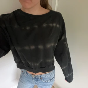 Svart sweatshirt med svagt tiedye mönster - Cool svart croppad sweatshirt med batik/tie dye mönster i ljusare toner. 