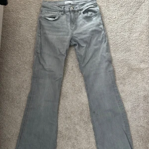 Grå bootcut jeans från Gina  - Snygga grå jeans från Diesel med klassisk femficksdesign och bootcut-ben. Jeansen har en låg midja och raka linjer som ger en chill vibe. Materialet är mjukt denim och färgen är neutral grå, perfekt för att matcha med olika stilar.