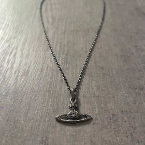 Vivienne Westwood halsband i silver - Snyggt halsband från Vivienne Westwood i silverfärgad metall med den ikoniska orb-berlocken. Kedjan är tunn och har ett diskret märke vid låset. Perfekt för dig som gillar statement-smycken med cool design och vill sticka ut lite extra.