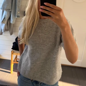 Grå stickad tröja med kort ärm☺️ - Mysig grå stickad tröja med korta ärmar och rund hals. Tröjan har en loose passform och är perfekt att slänga på sig till jeans. Materialet är mjukt och fluffigt, vilket gör den extra skön att bära under kyliga dagar.
