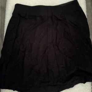 Svart kortkjol från Pull&Bear - En stilren svart kortkjol från Pull&Bear i storlek S. Kjolen har en enkel och klassisk design med rak passform och bred linning. Perfekt att matcha med en cool t-shirt eller hoodie för en chill look.