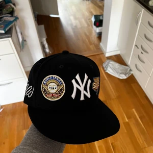 New York Yankees svart keps World Series - Svart/mörkblå New Era keps med New York Yankees logga framtill och broderade World Series märken i guld, blått och vitt. Platt skärm och klassisk baseballstil, perfekt för dig som gillar sport och streetwear. Hör av dig vid funderingar om kepsen. Storlek 7/55,8 cm