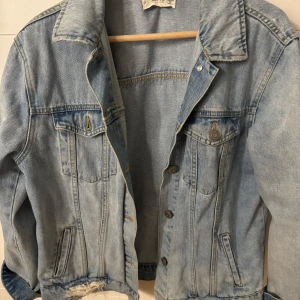 Ljusblå jeansjacka från Mango - Snygg ljusblå jeansjacka från Mango med klassisk krage, knappar framtill och två bröstfickor med lock. Jackan har slitna detaljer vid nederkant och ärmar för en cool vibe. Perfekt att slänga över en hoodie eller t-shirt för en chill look.