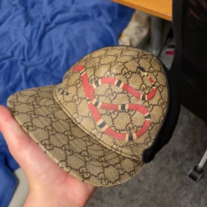 Gucci keps med orm och GG-mönster - Tjena säljer/byter min Gucci snake keps, letar helst efter byten men funkar pengar, det är bara att skriva för fler bilder eller frågor, ja kepsen är äkta, har den svarta lappen med som ska sitta på högra sidan det ser ni på bild 4. Kan gå ner i pris vid snabb affär.