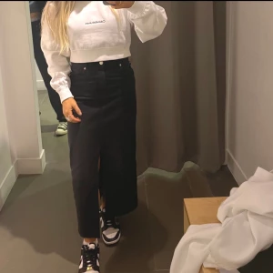 Svart lång jeanskjol med slits - ”Urtvättad svart” kjol med en slits framtill. Stretchigt jeans-material. Är i mycket bra skick. Har lätta konstgjorda slitningar nertill. Säljer pga att den tyvärr inte kommer till användning. 